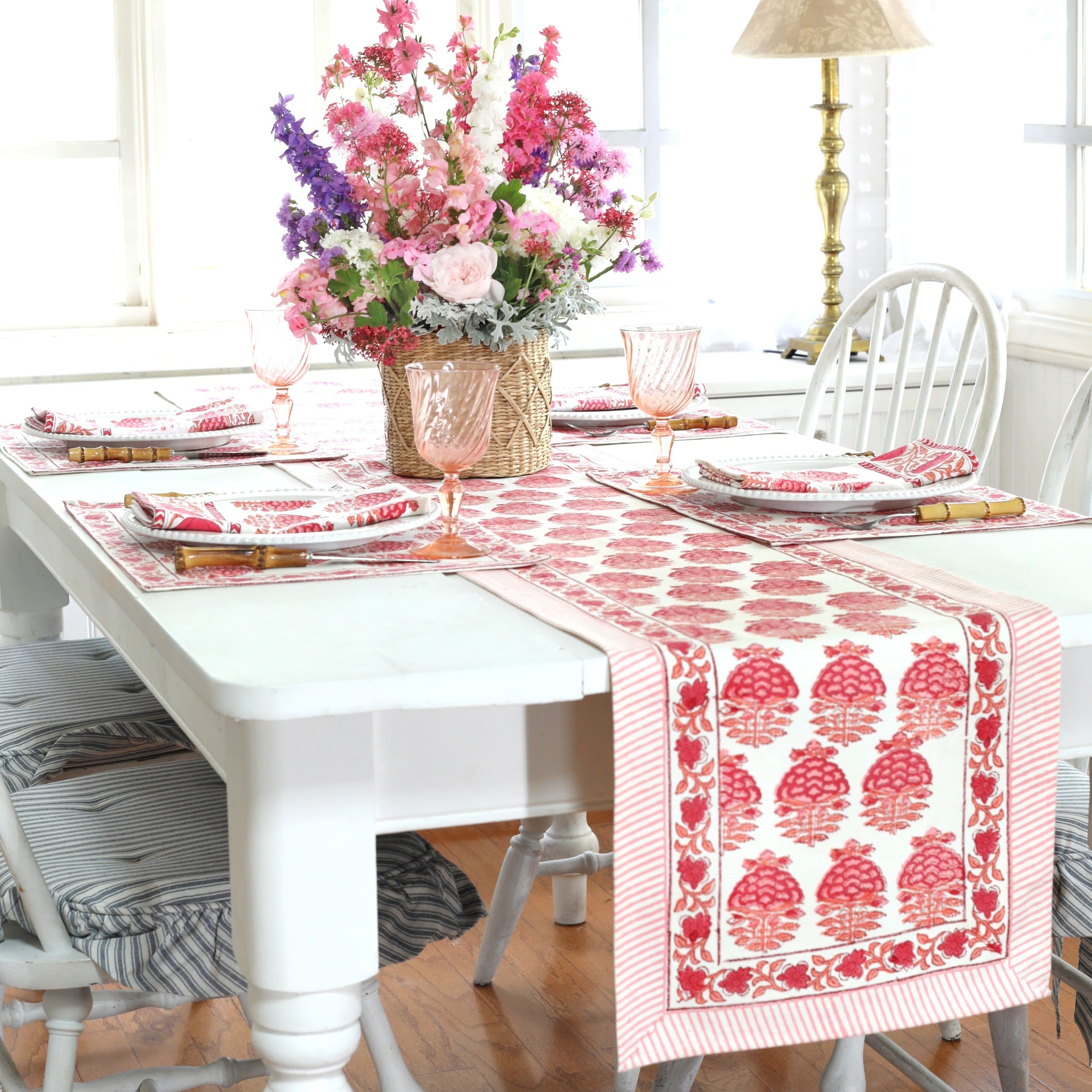 Dining room table set with a floral centerpiece, red patterned table runner, and white chairs.
