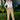 Woman wearing a white top and colorful pants standing outdoors with greenery around.