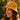 A woman wearing a yellow patterned bucket hat with red and green floral motifs, photographed outdoors against a warm, sunlit green background.