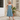 Woman wearing a blue patterned dress standing in front of a building with shutters.